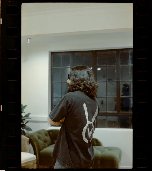 A real film photograph of the VAURA tee worn in a studio, with its white back symbol visible